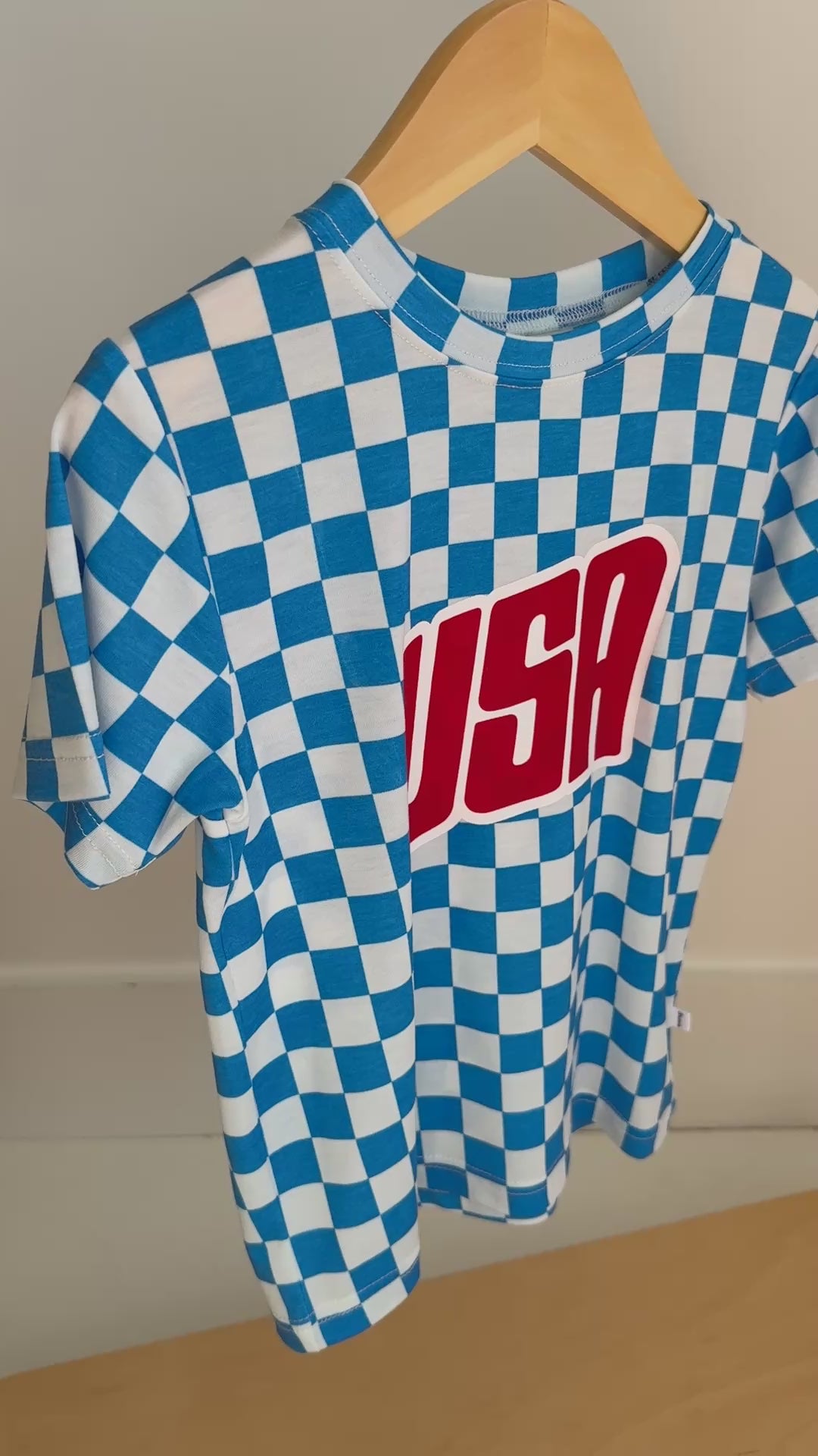 Blue and white checkered t-shirt with 'USA' print hanging on a rack