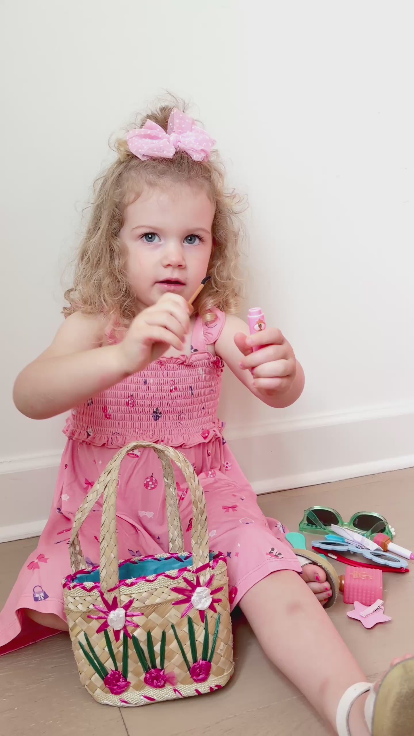Video of a young girl in a pink dress sitting on a surface playing with girly toys