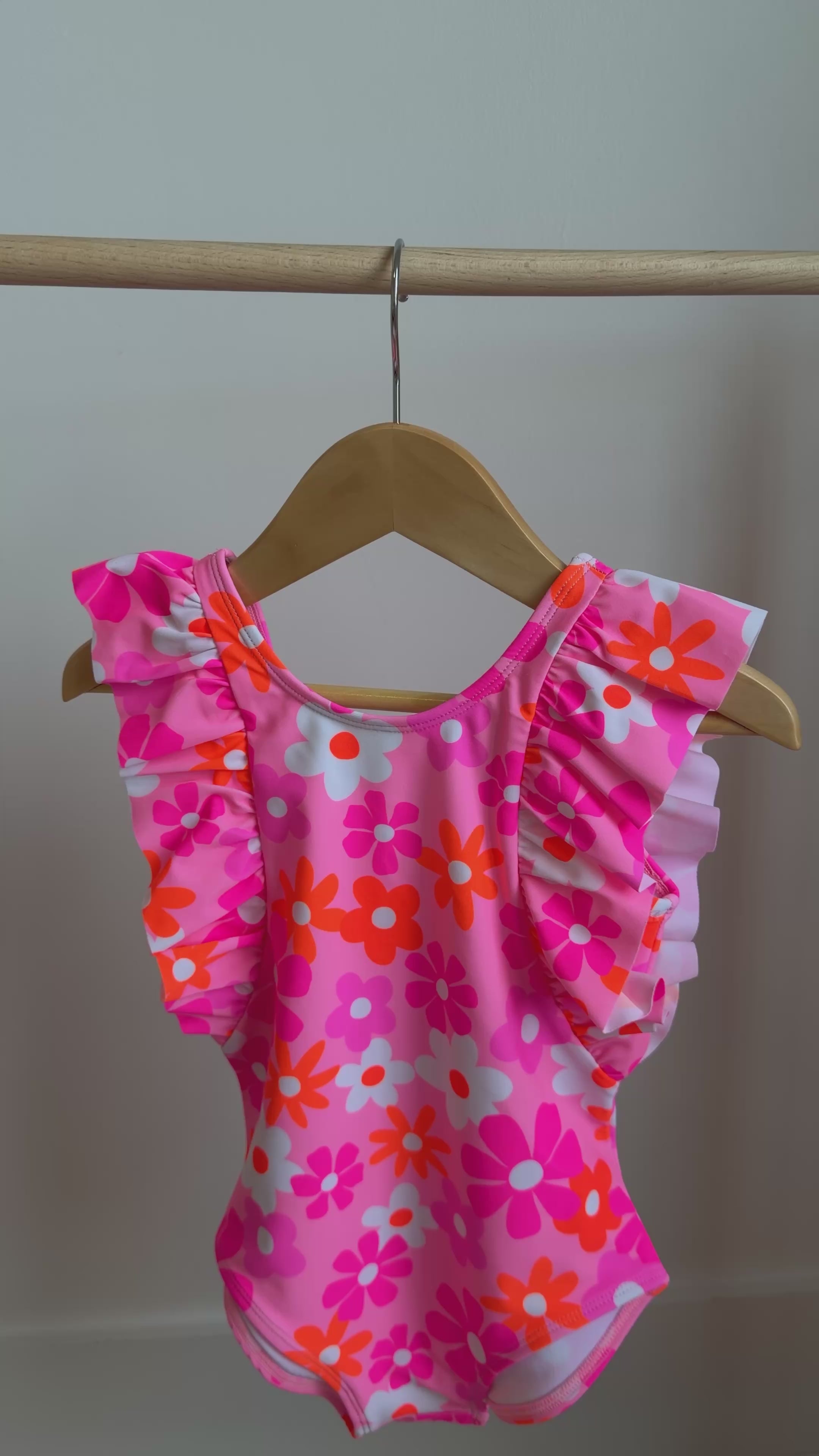 Pink floral swimsuit with ruffles hanging on a rack