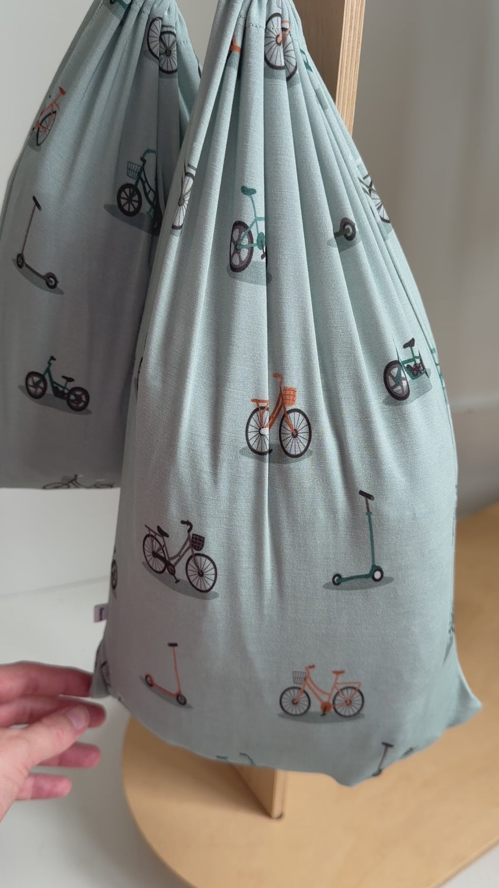 Video of fitted sheets featuring small vehicle patterns on a light blue background hanging inside a bag placed on a rack