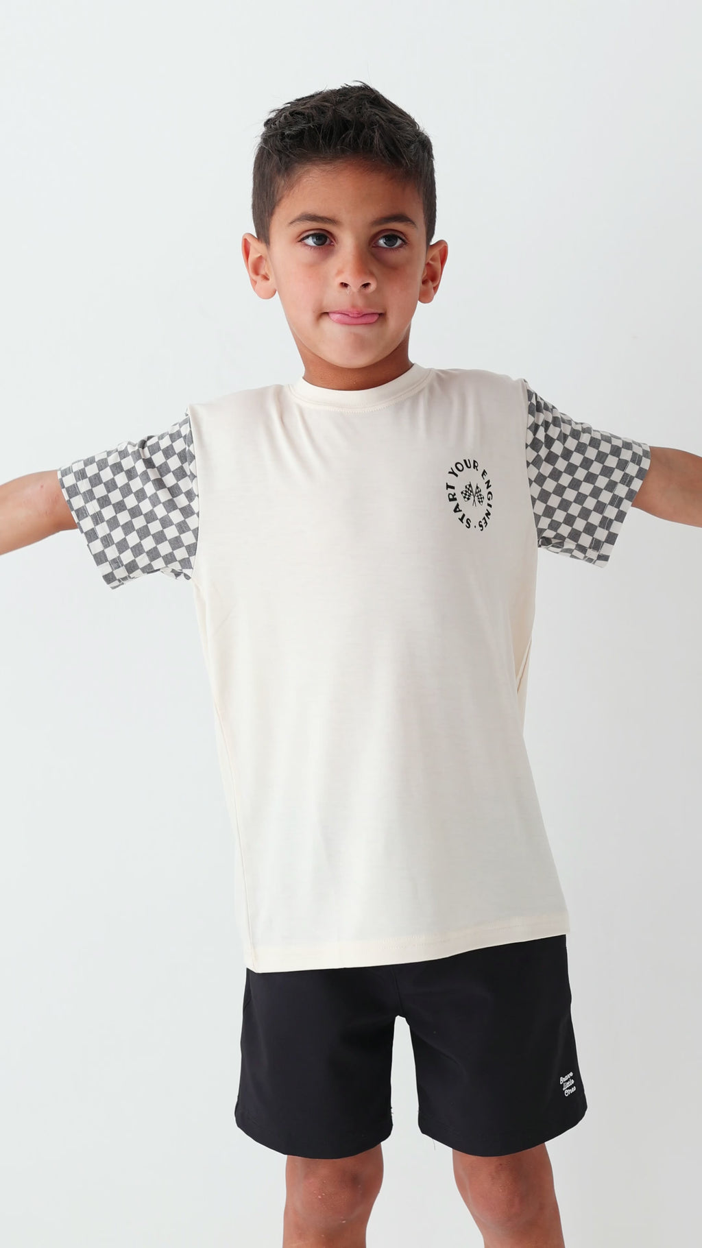 Child wearing a white t-shirt with checkered sleeves and black shorts on a white background