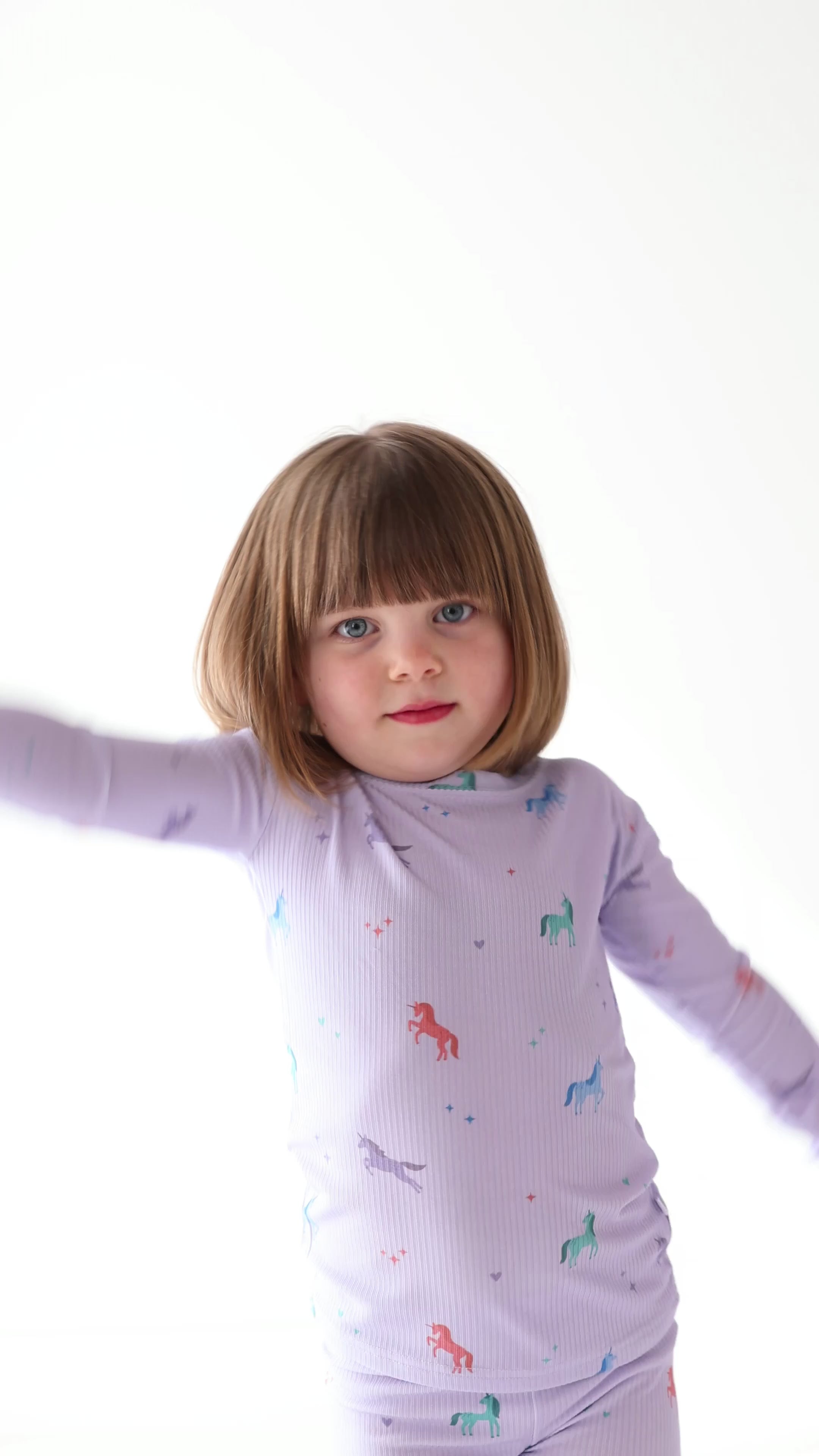 Video of a child wearing a purple pajama set with unicorn prints on a white background