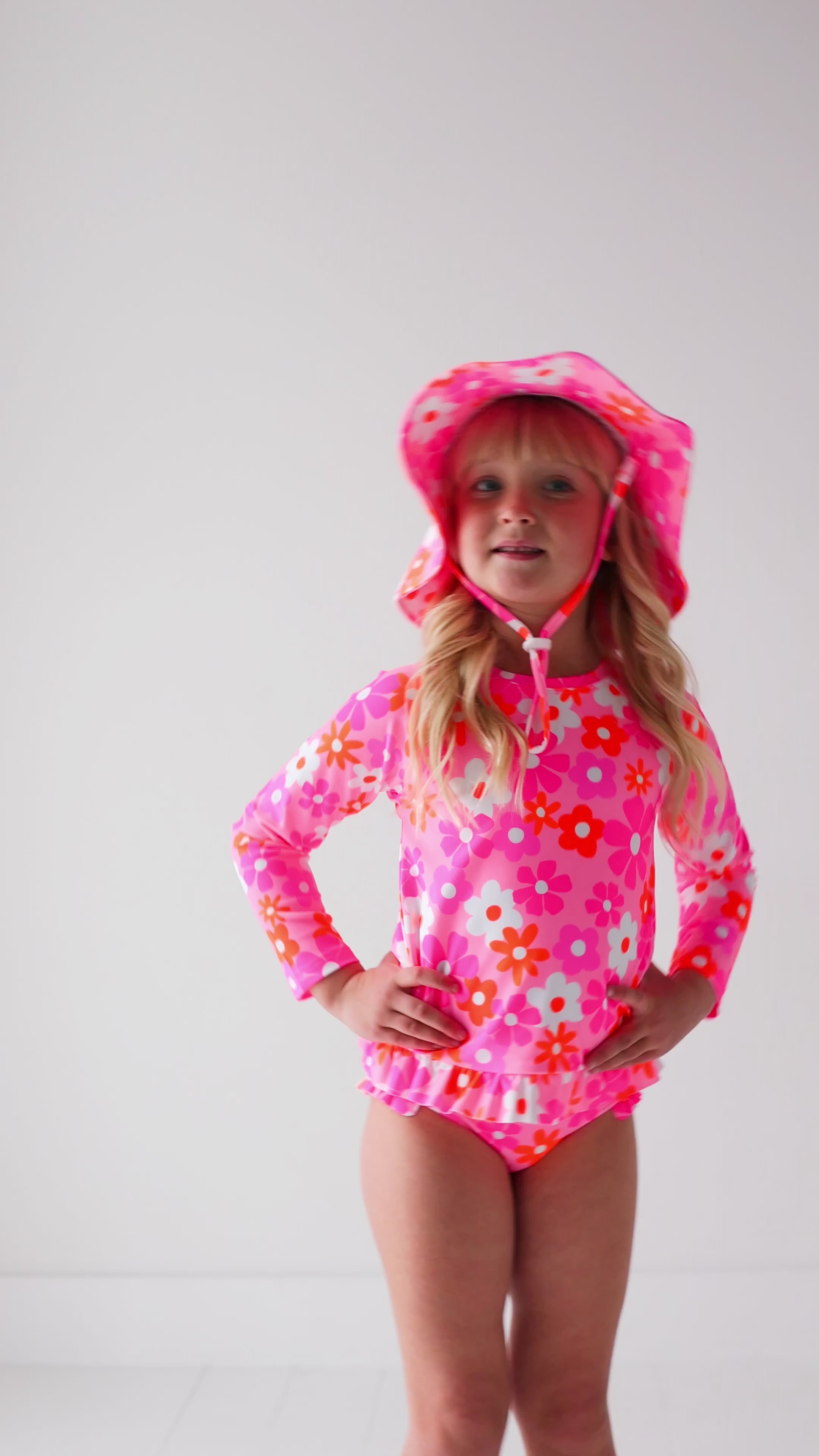 Child wearing a pink floral two-piece swimsuit and a matching sun hat on a white background