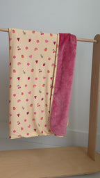 Baby blanket with colorful fruit pattern on one side and solid color on the other draped over a wooden rack