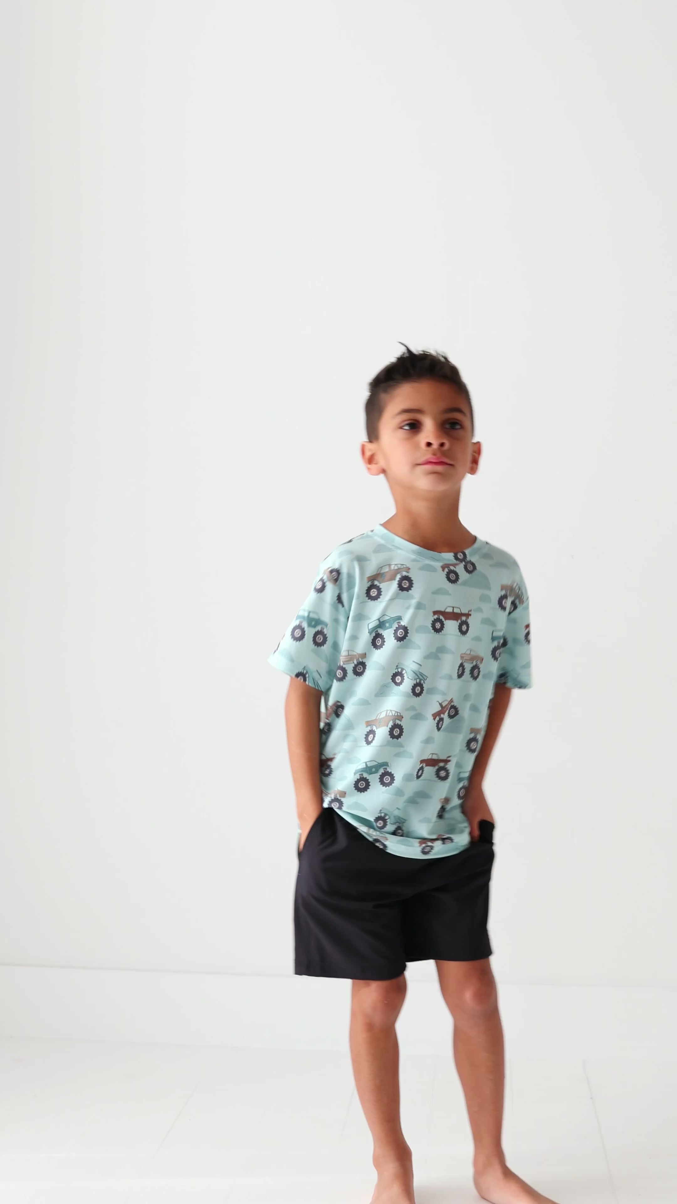 Child wearing a light blue t-shirt with vehicle pattern and black shorts on a white background