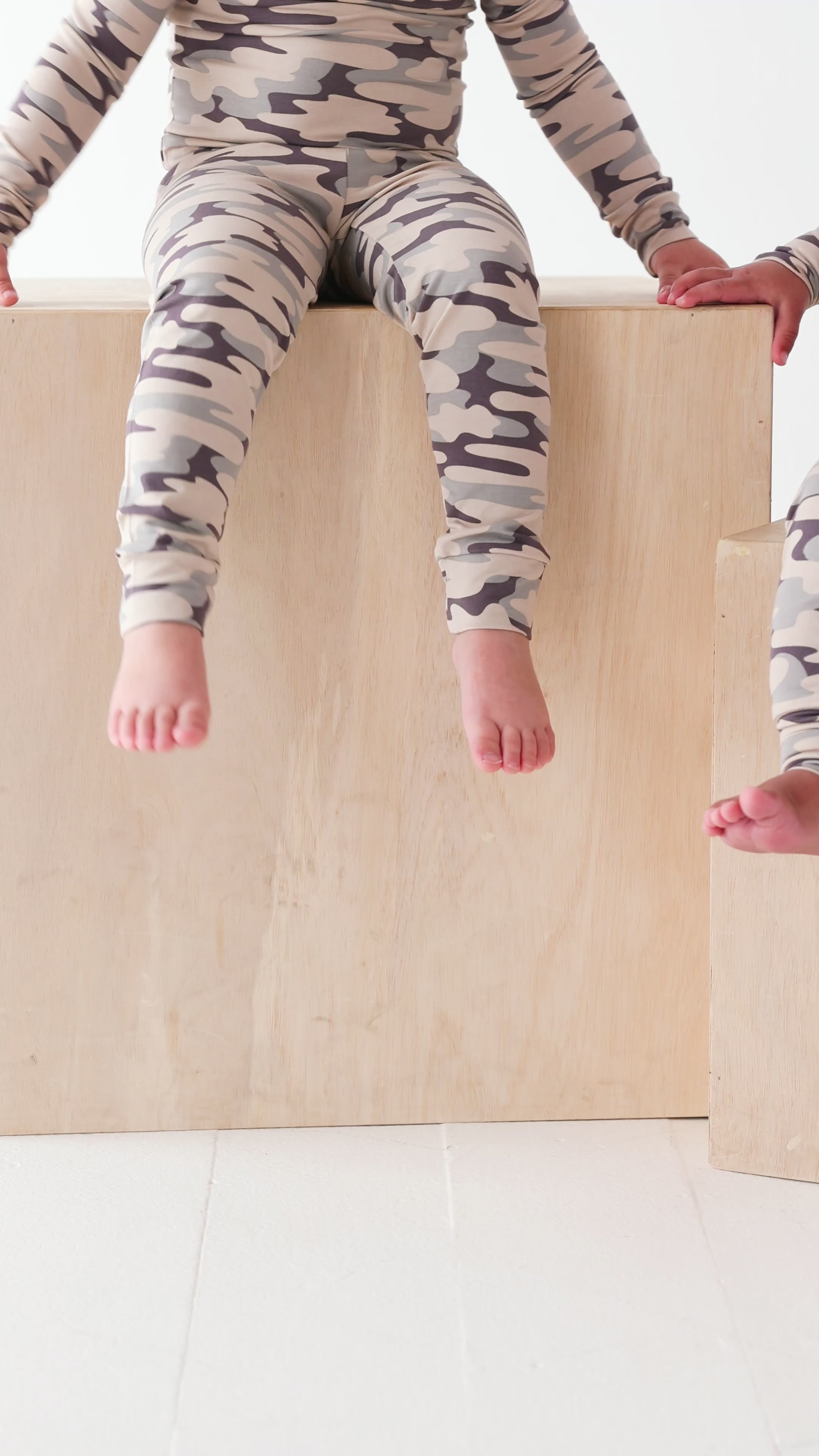 Video of two children wearing matching camouflage pajamas sitting on a white background