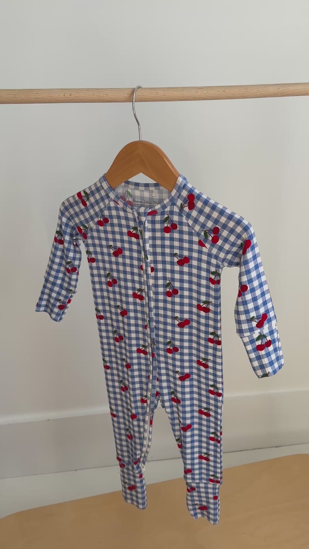 Video of a children's onesie with blue checkered pattern and red cherries hanging on a rack