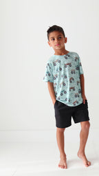 Child wearing a light blue t-shirt with vehicle patterns and black shorts on a white background