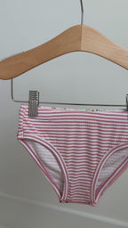Set of three children's underwear with floral, strawberry, and striped patterns hanging on a rack