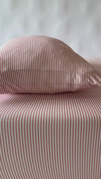 Bed with pink striped bedding and a wooden frame on a plain background