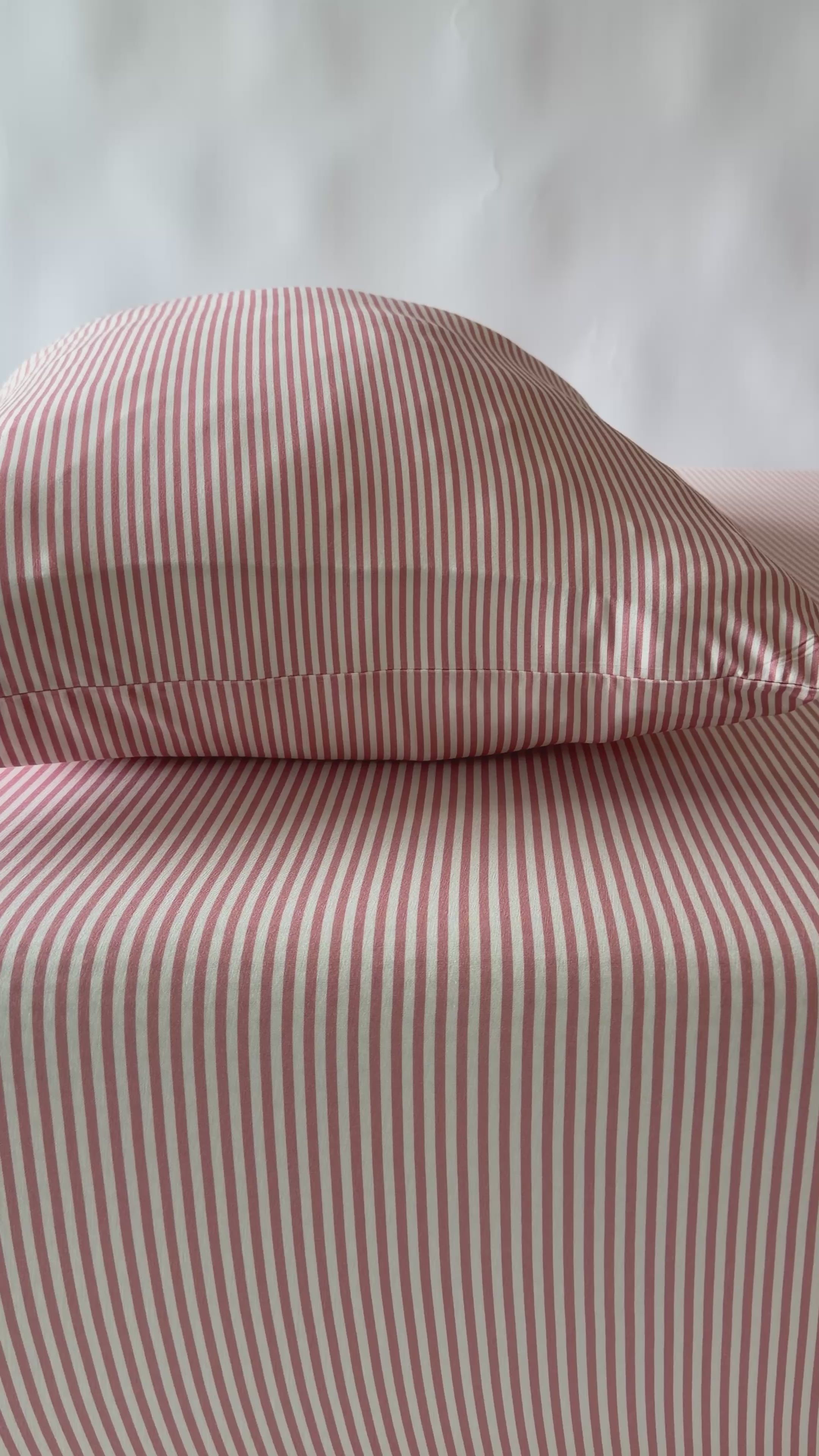 Bed with pink striped bedding and a wooden frame on a plain background