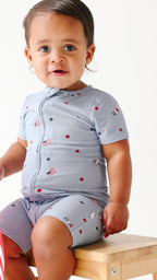 Child wearing a short romper with American-themed pattern sitting on a wooden stool.