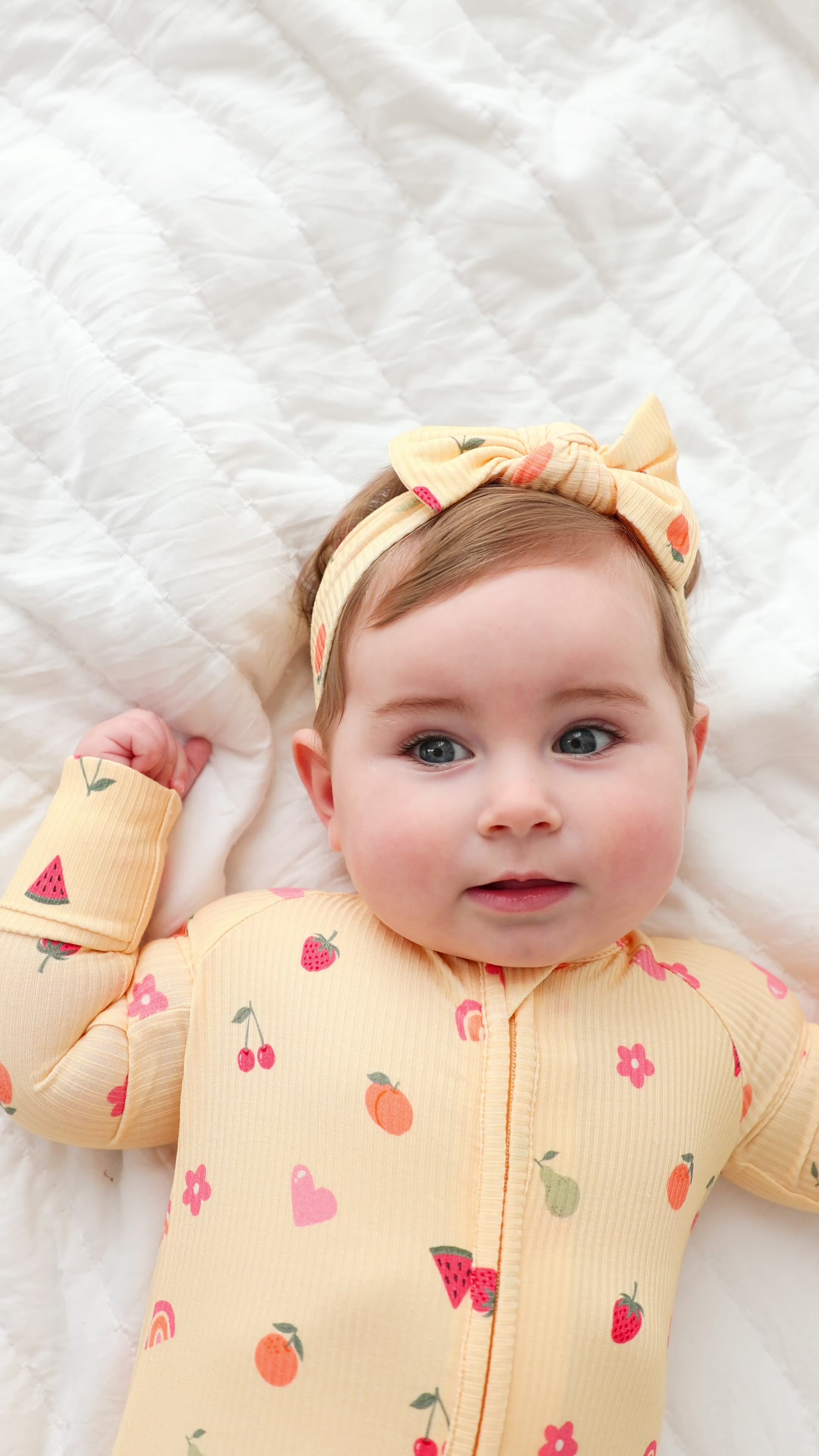 Baby wearing a yellow outfit with fruits patterns and a matching headband on a white background