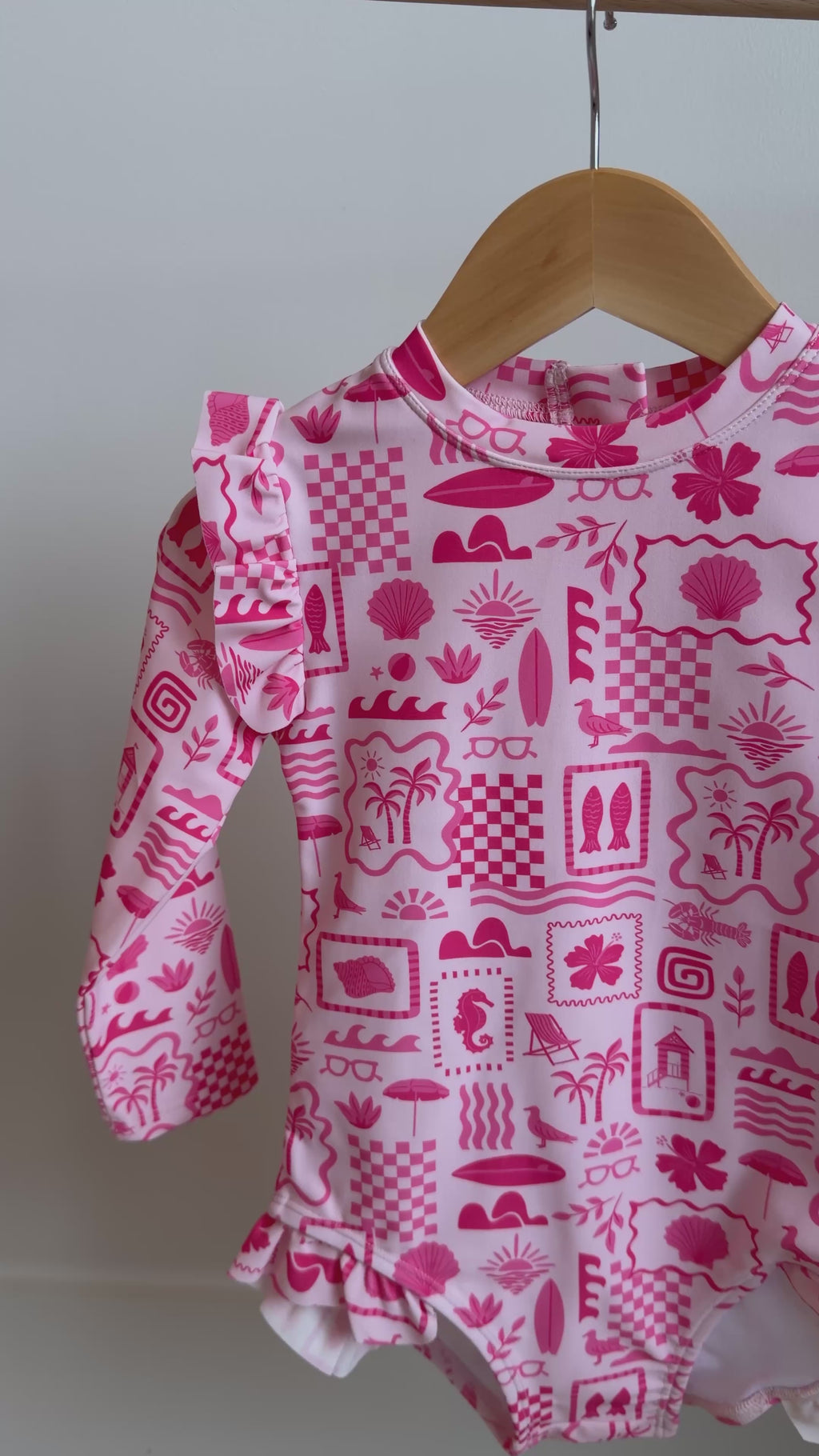 Pink and white patterned long sleeve one-piece swimsuit hanging on a rack