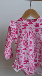 Pink and white patterned long sleeve one-piece swimsuit hanging on a rack