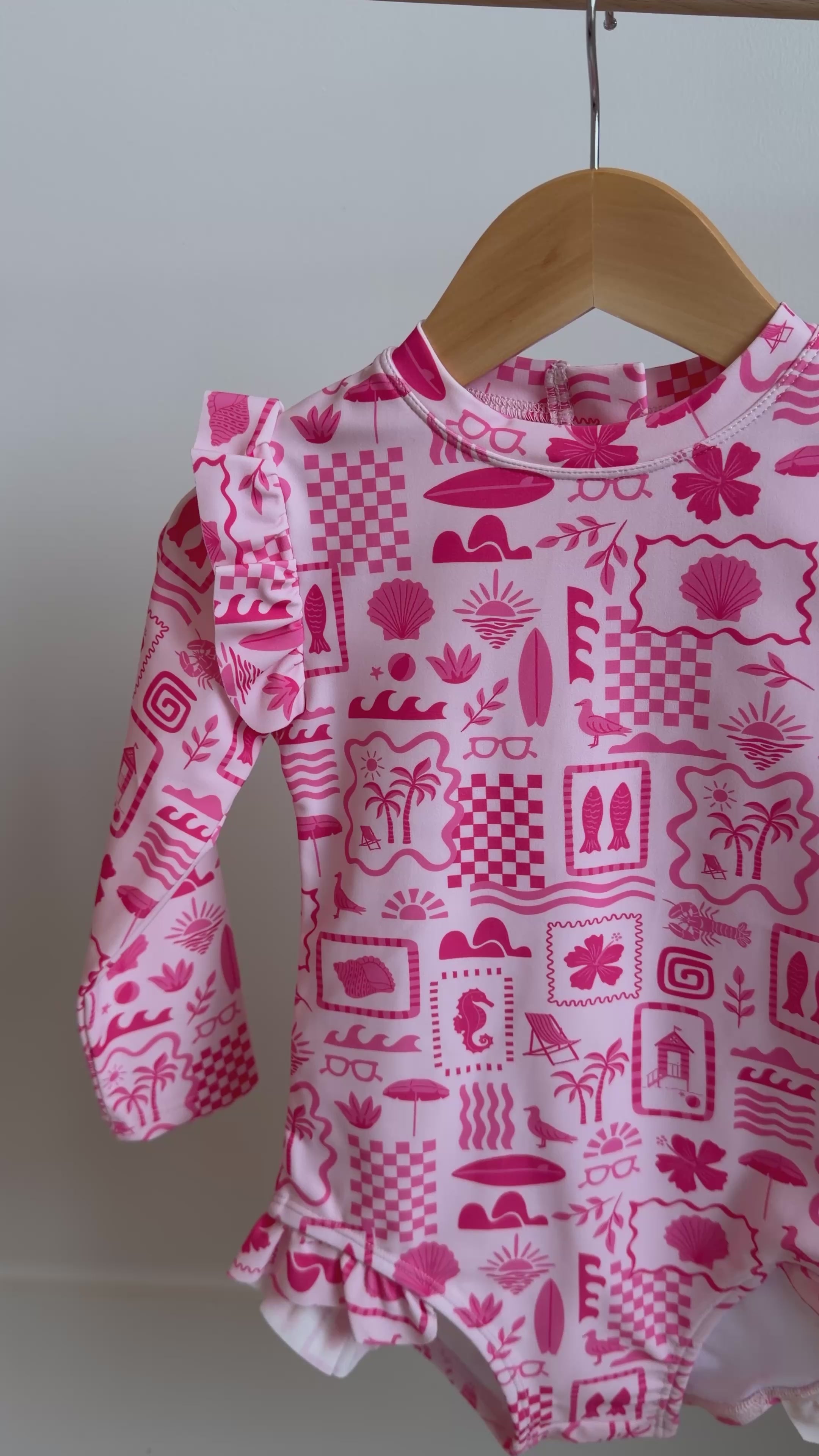 Pink and white patterned long sleeve one-piece swimsuit hanging on a rack
