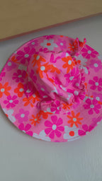 Floral patterned sun hat with a strap on a plain background
