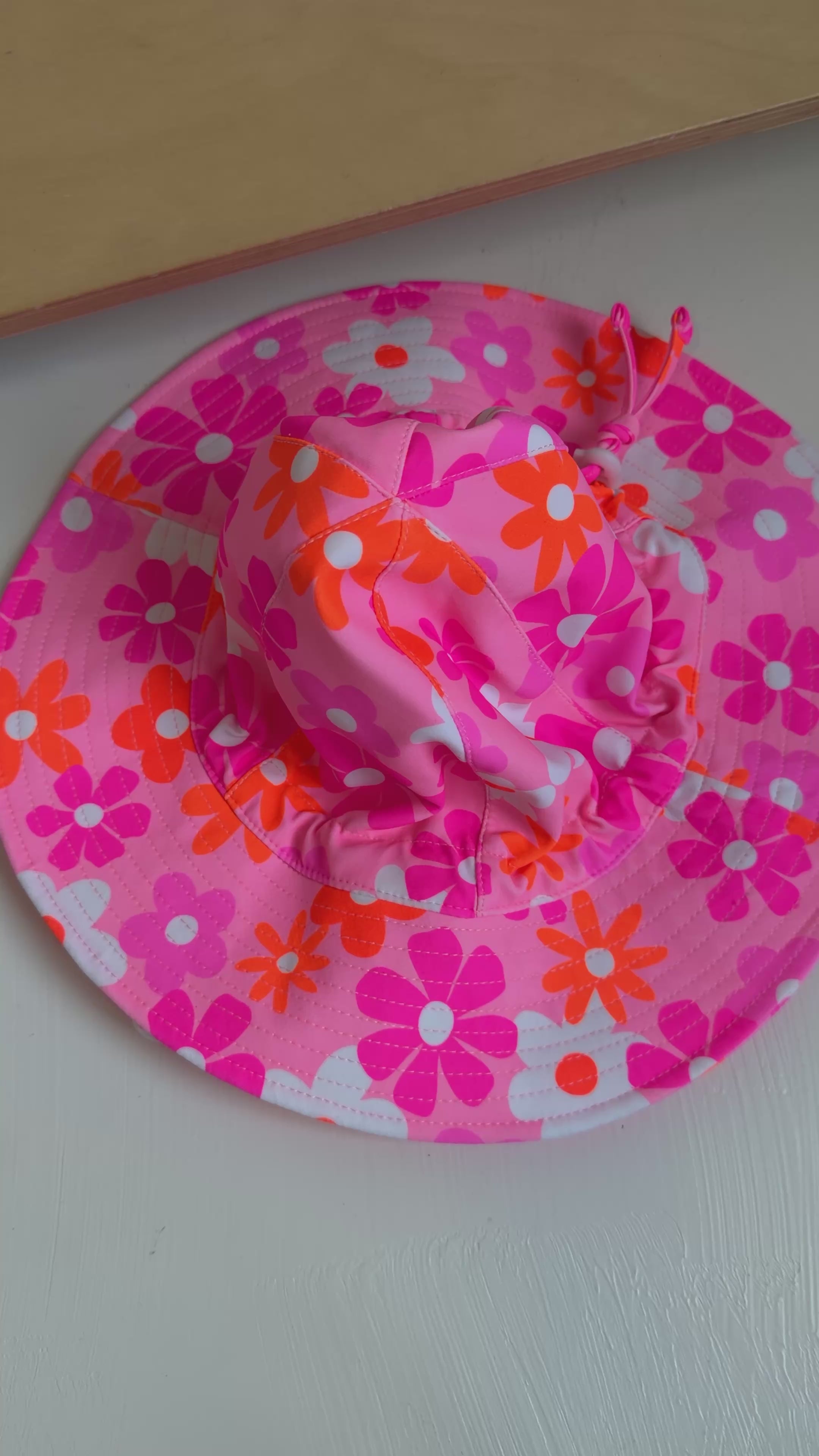 Floral patterned sun hat with a strap on a plain background