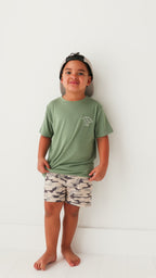 Child wearing a green t-shirt, taupe cap and camouflage shorts on a white background