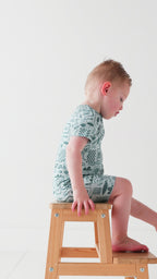 Child wearing a blue short romper with summer patterns sitting on a stool