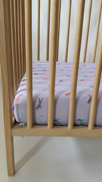 Crib with a fitted sheet featuring colorful unicorn patterns on a light background