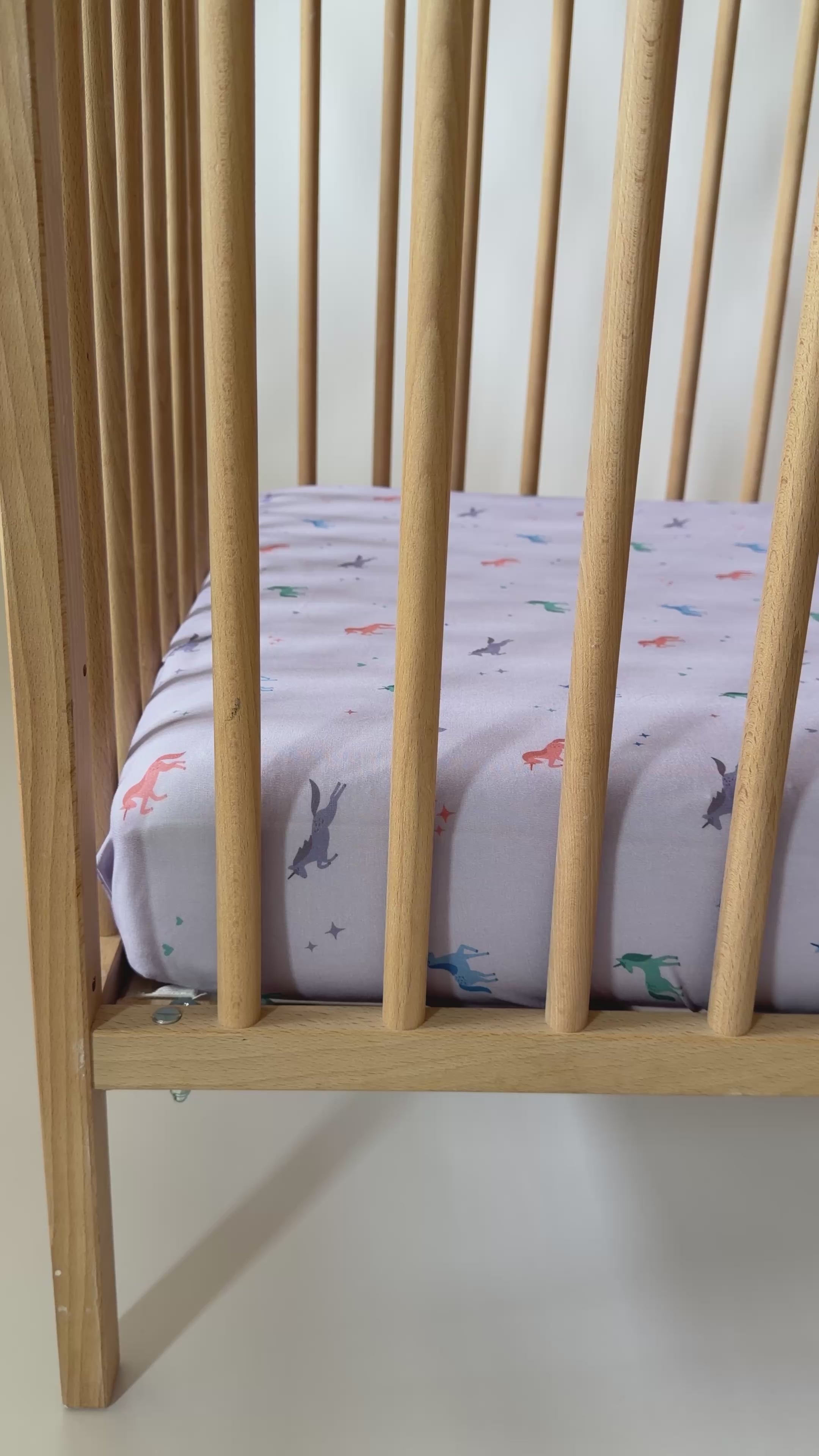 Crib with a fitted sheet featuring colorful unicorn patterns on a light background