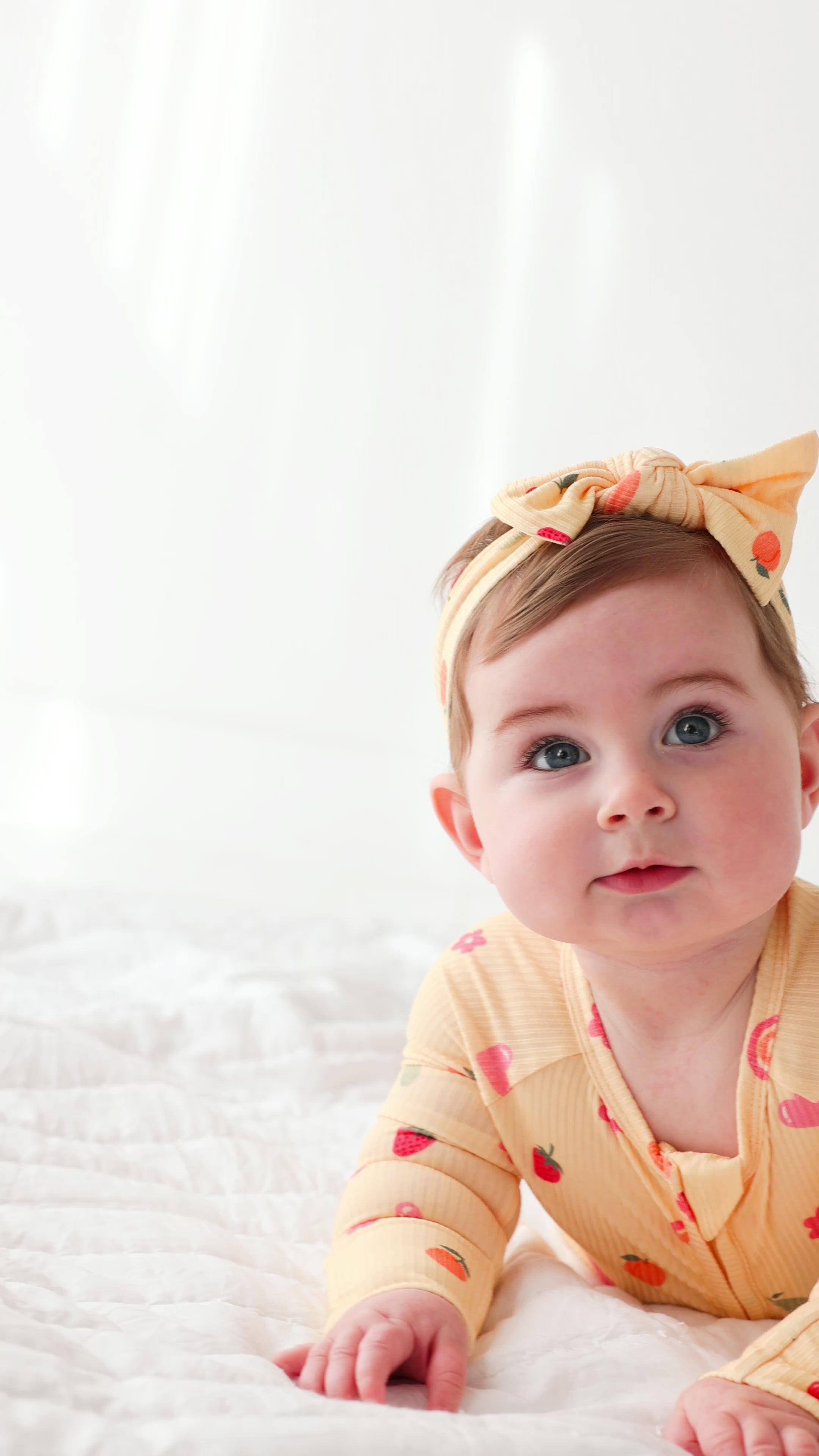 Baby wearing a yellow outfit with fruits patterns and a matching headband on a white background