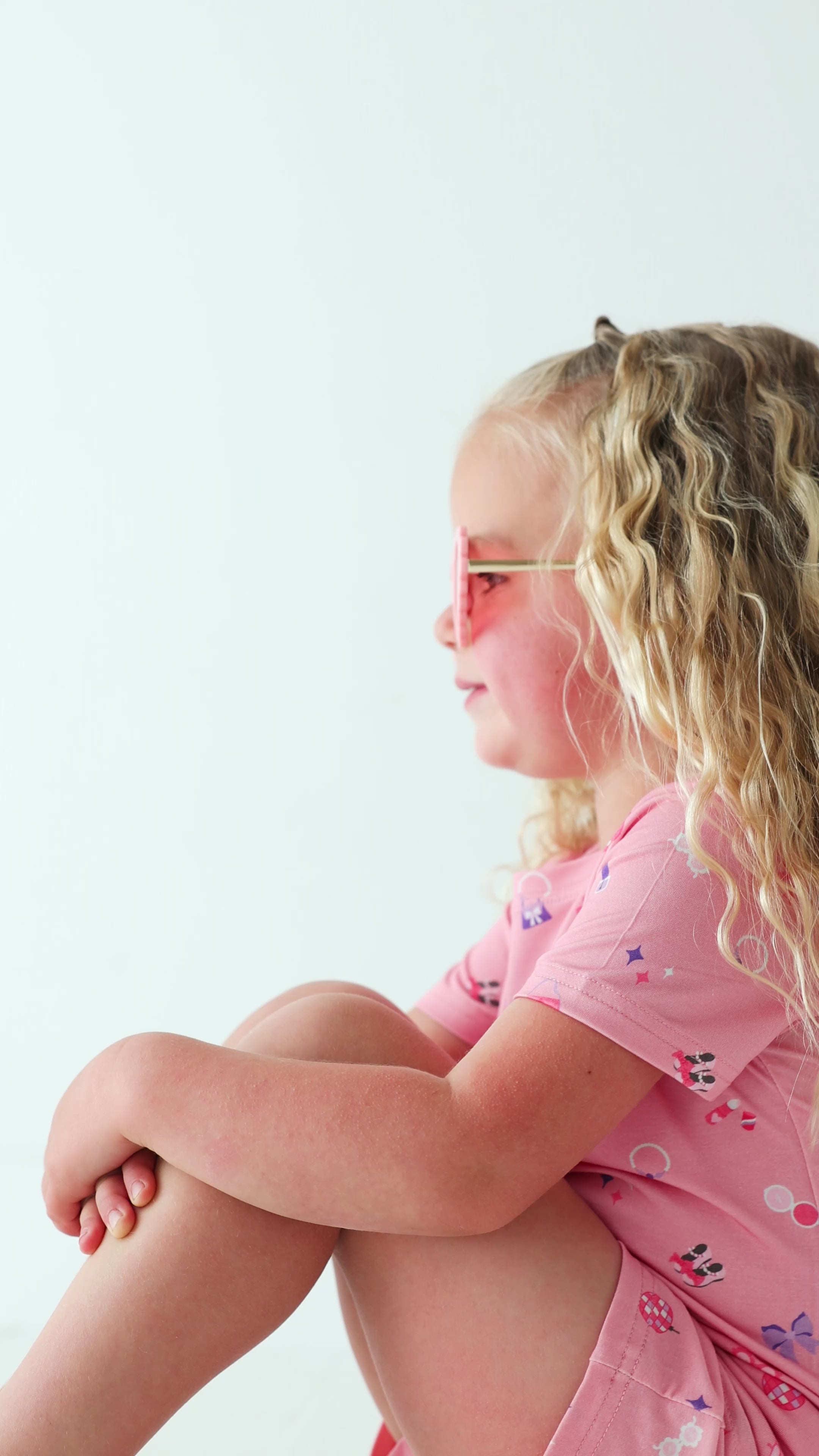 Video of a child wearing a pink shorts pajama set with heart sunglasses on a white background