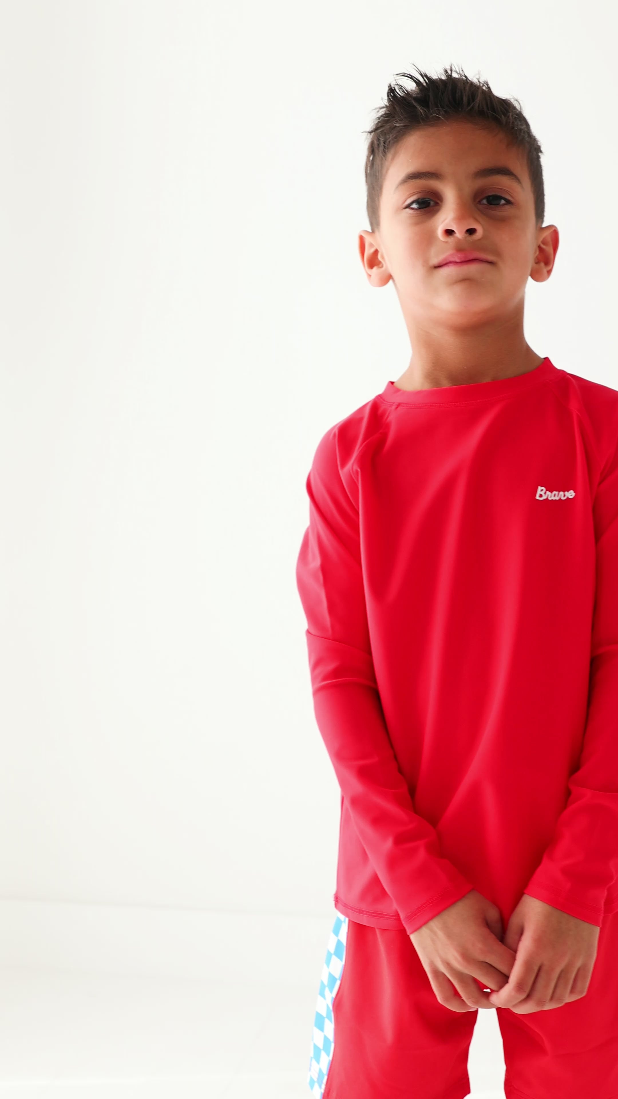 Child wearing a red rash guard and matching red swim trunks on a white background