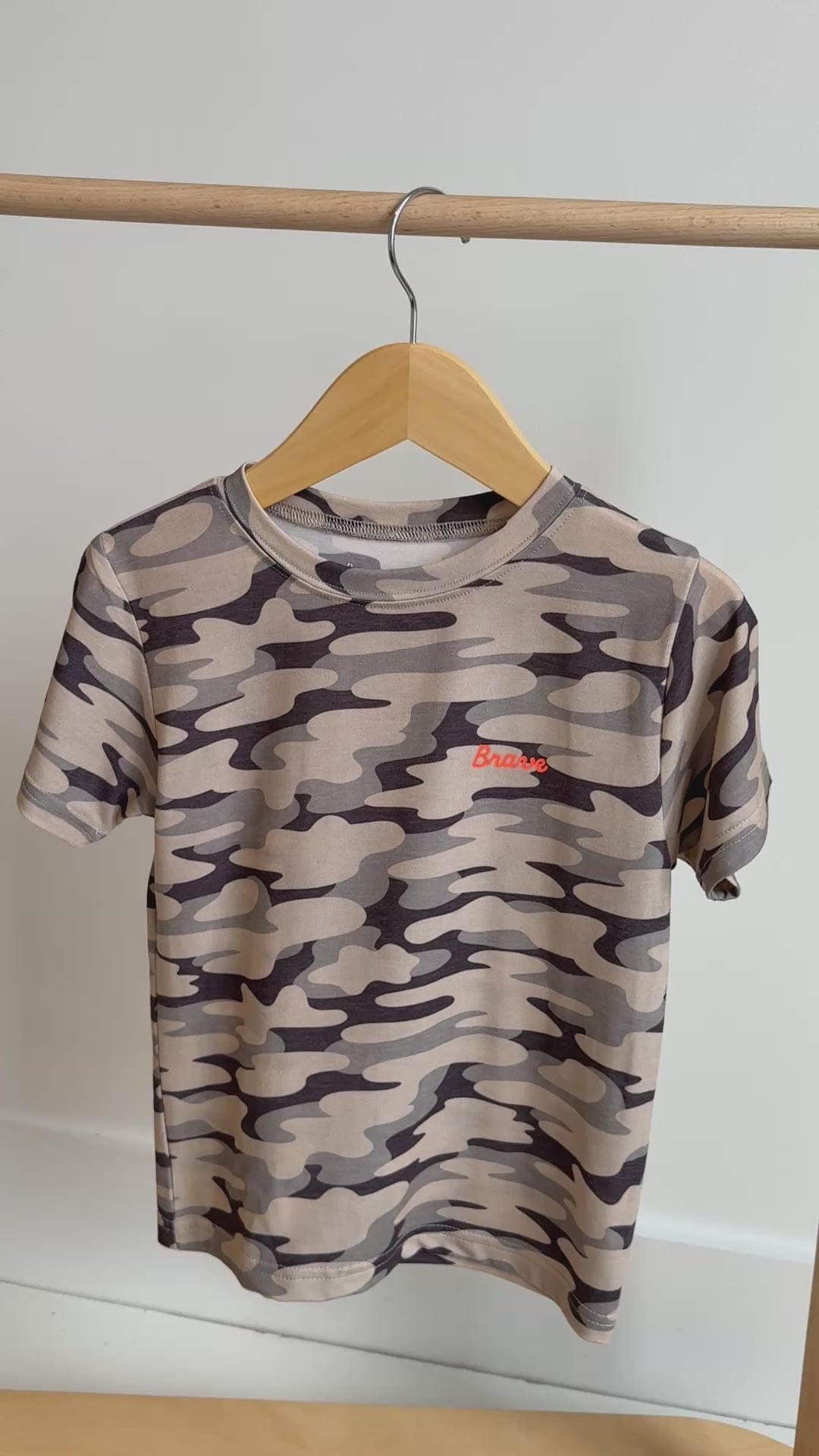 Camouflage-patterned t-shirt with a brand logo hanging on a rack