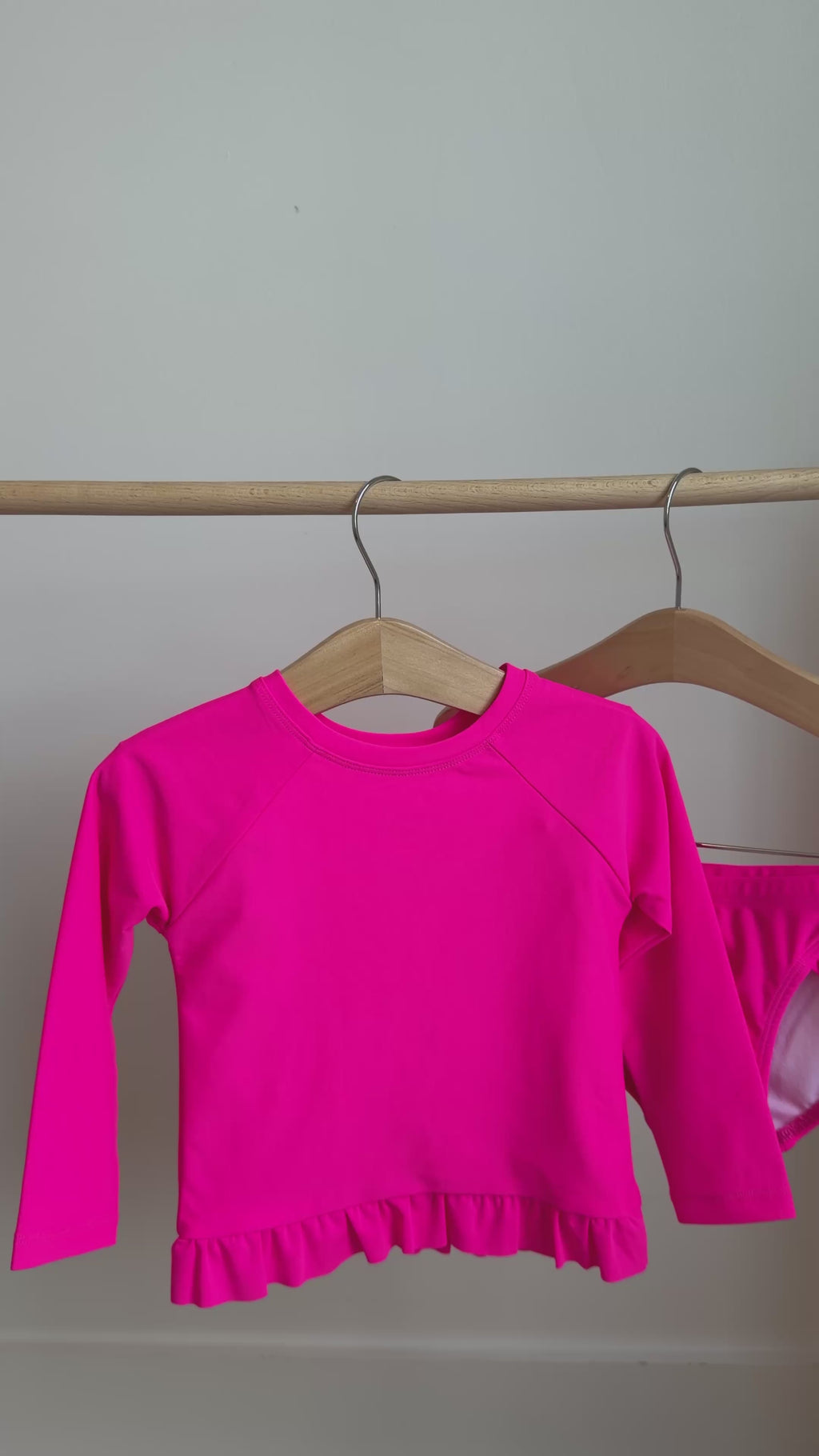 A bright pink long sleeve two-piece swimsuit hanging on a rack