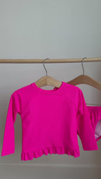 A bright pink long sleeve two-piece swimsuit hanging on a rack