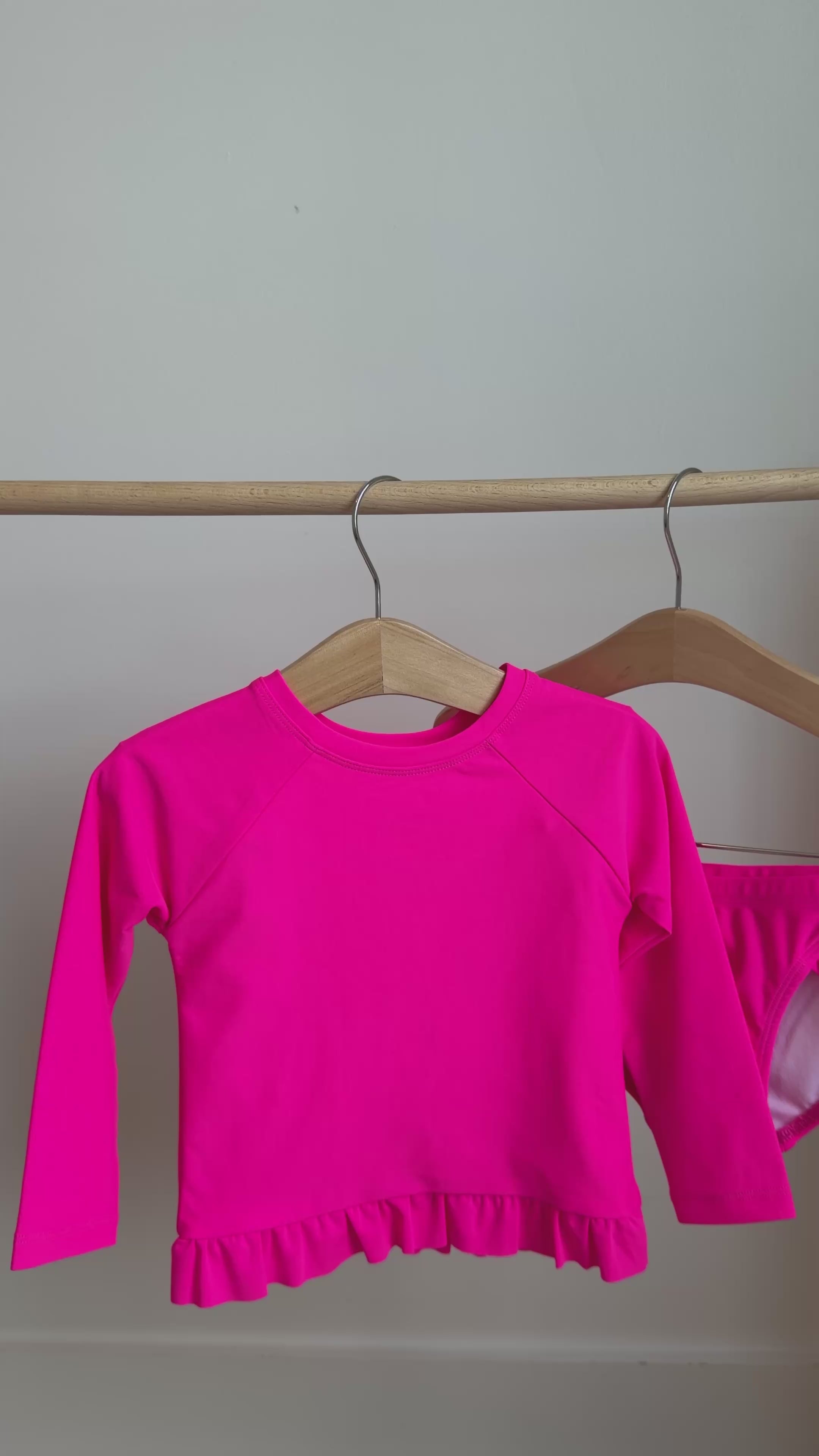 A bright pink long sleeve two-piece swimsuit hanging on a rack