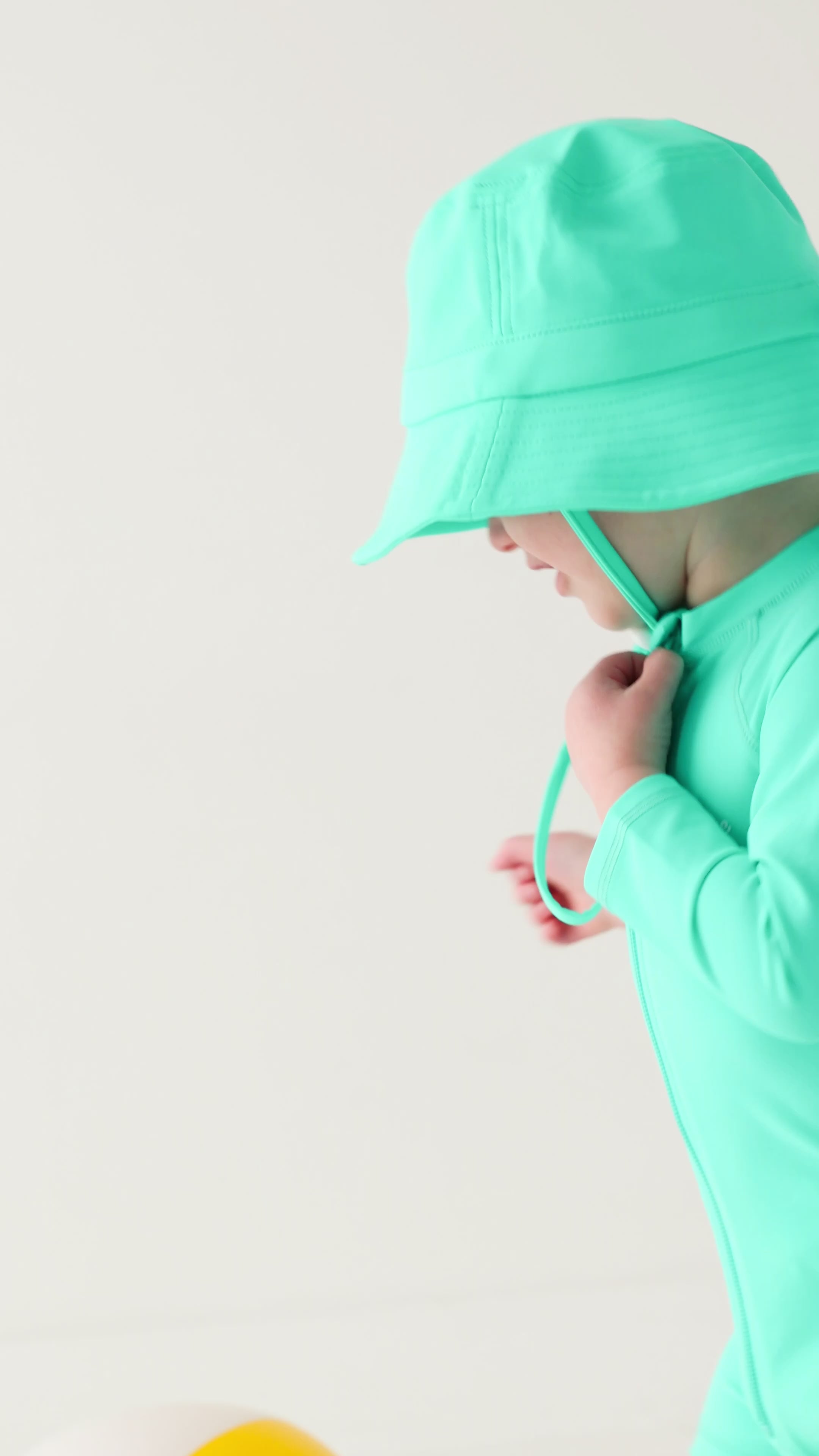 Child wearing a turquoise boy swimsuit and matching bucket hat on a white background