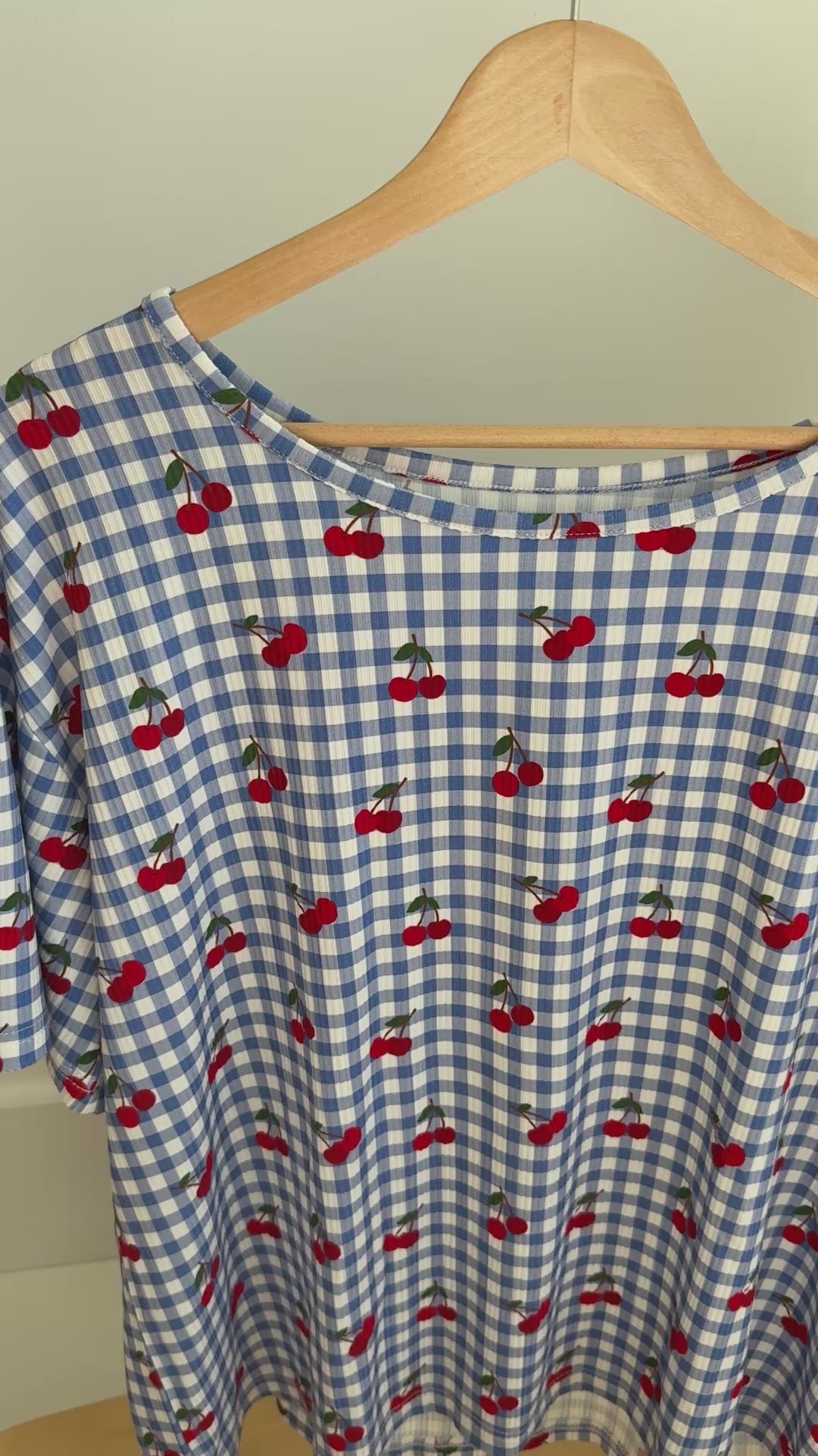 Video of a blue checkered pajama top with red cherries pattern hanging on a rack
