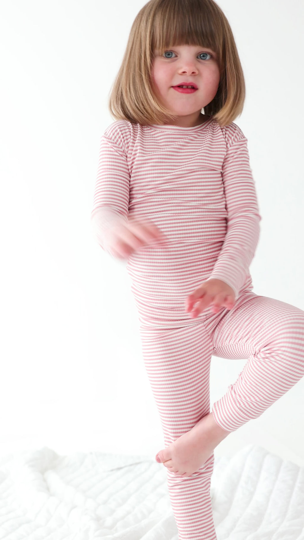 Child wearing a pink striped long sleeve pajama set on a white background