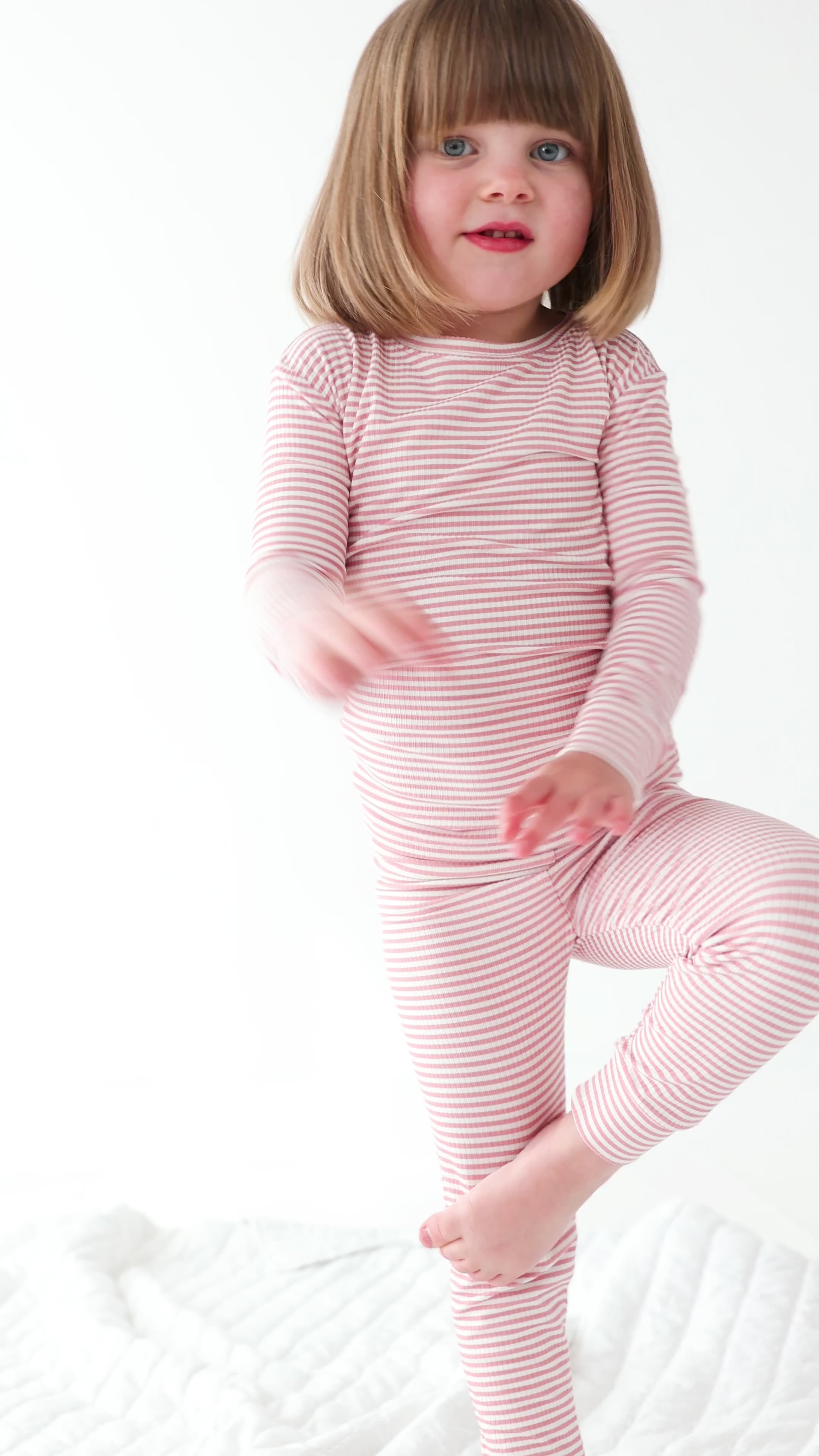 Child wearing a pink striped long sleeve pajama set on a white background