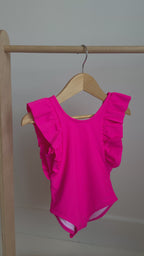 Bright pink one-piece swimsuit with ruffles hanging on a rack