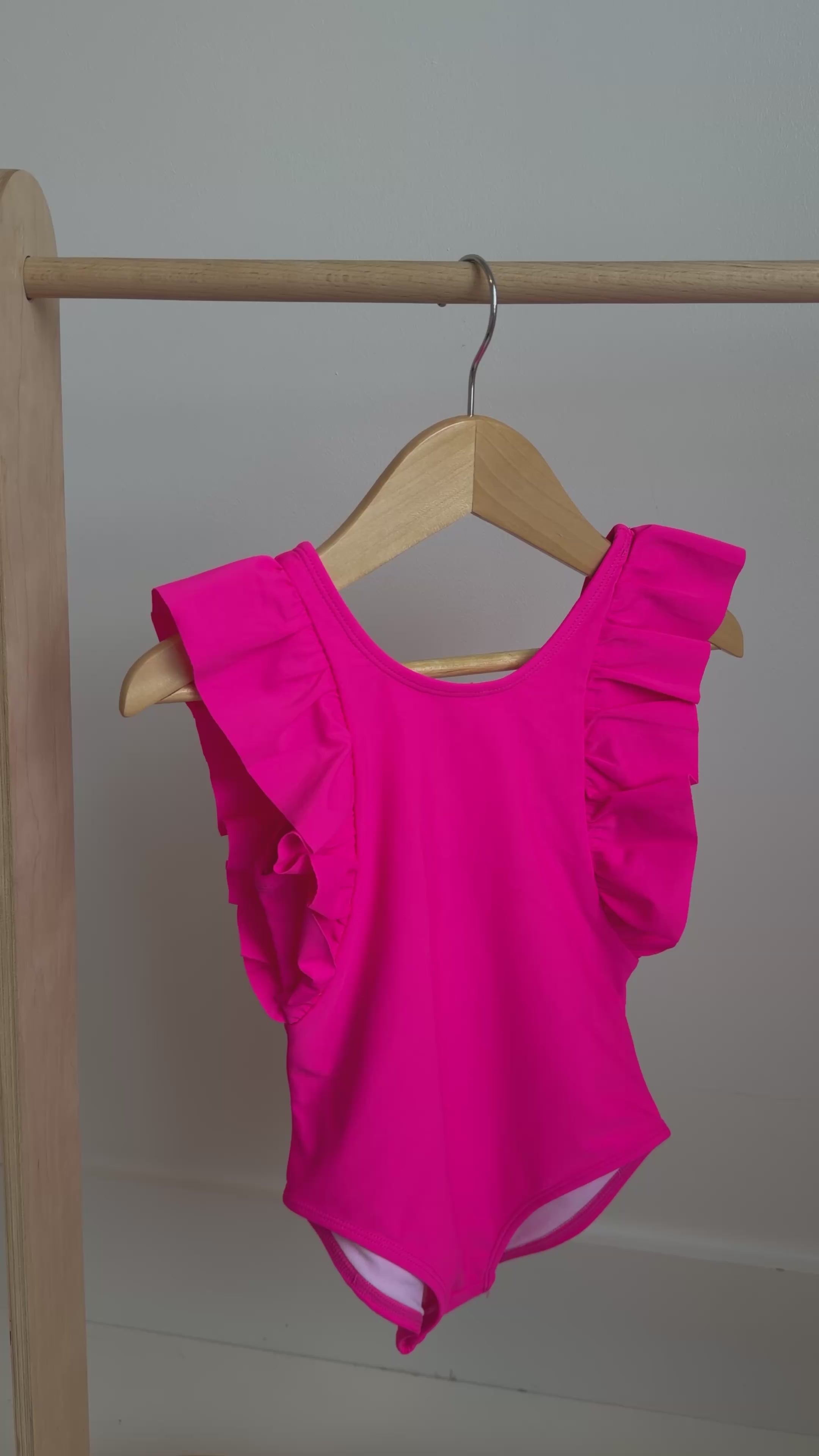 Bright pink one-piece swimsuit with ruffles hanging on a rack