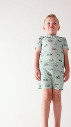 Child wearing a light blue outfit with bicycles & scooter patterns on a plain background