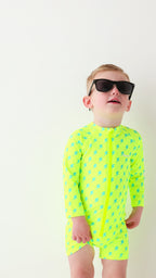 Child wearing a bright yellow boy swimsuit with a lightning bolt pattern and sunglasses on a white background