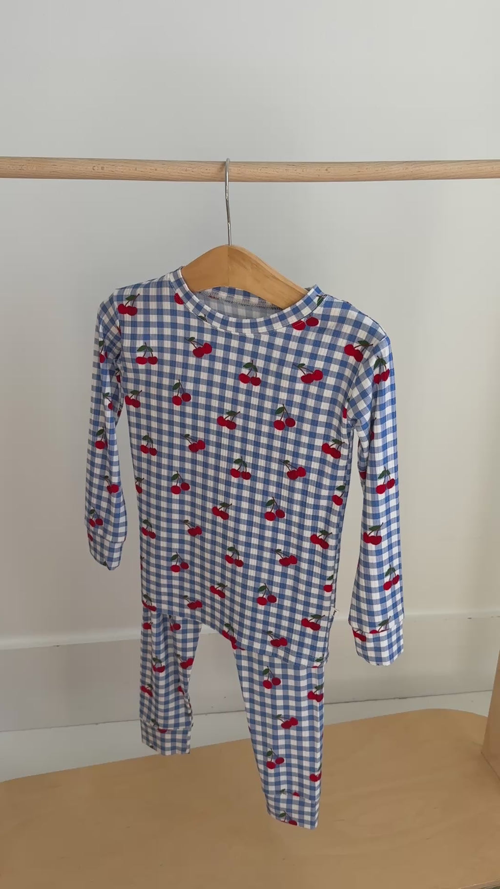 Children's pajama set with blue gingham pattern and red cherries hanging on a rack