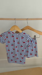 Video of a children's pajama set with blue gingham pattern and red cherries hanging on a rack