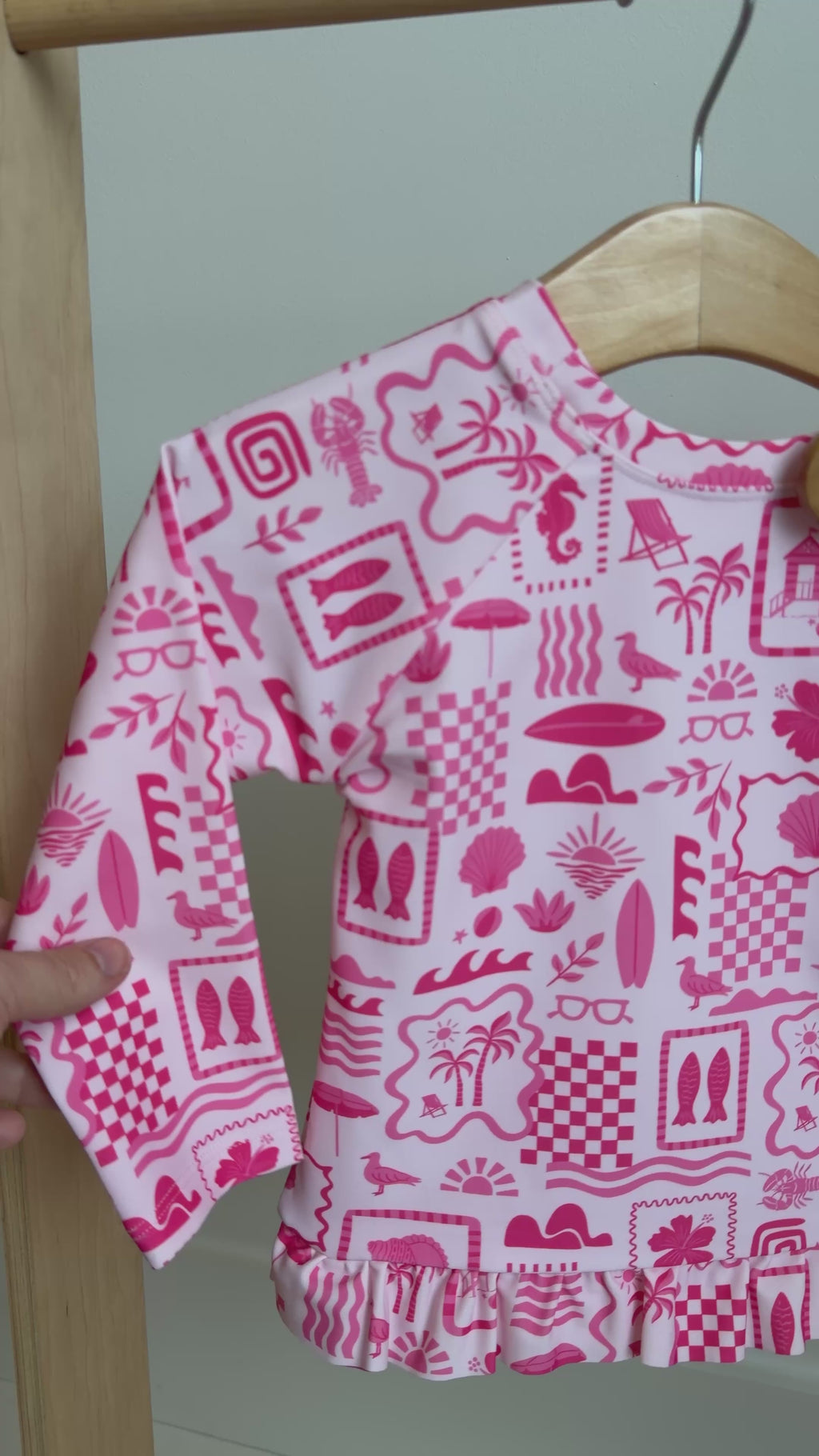 Pink and white patterned long sleeve two-piece swimsuit hanging on a rack