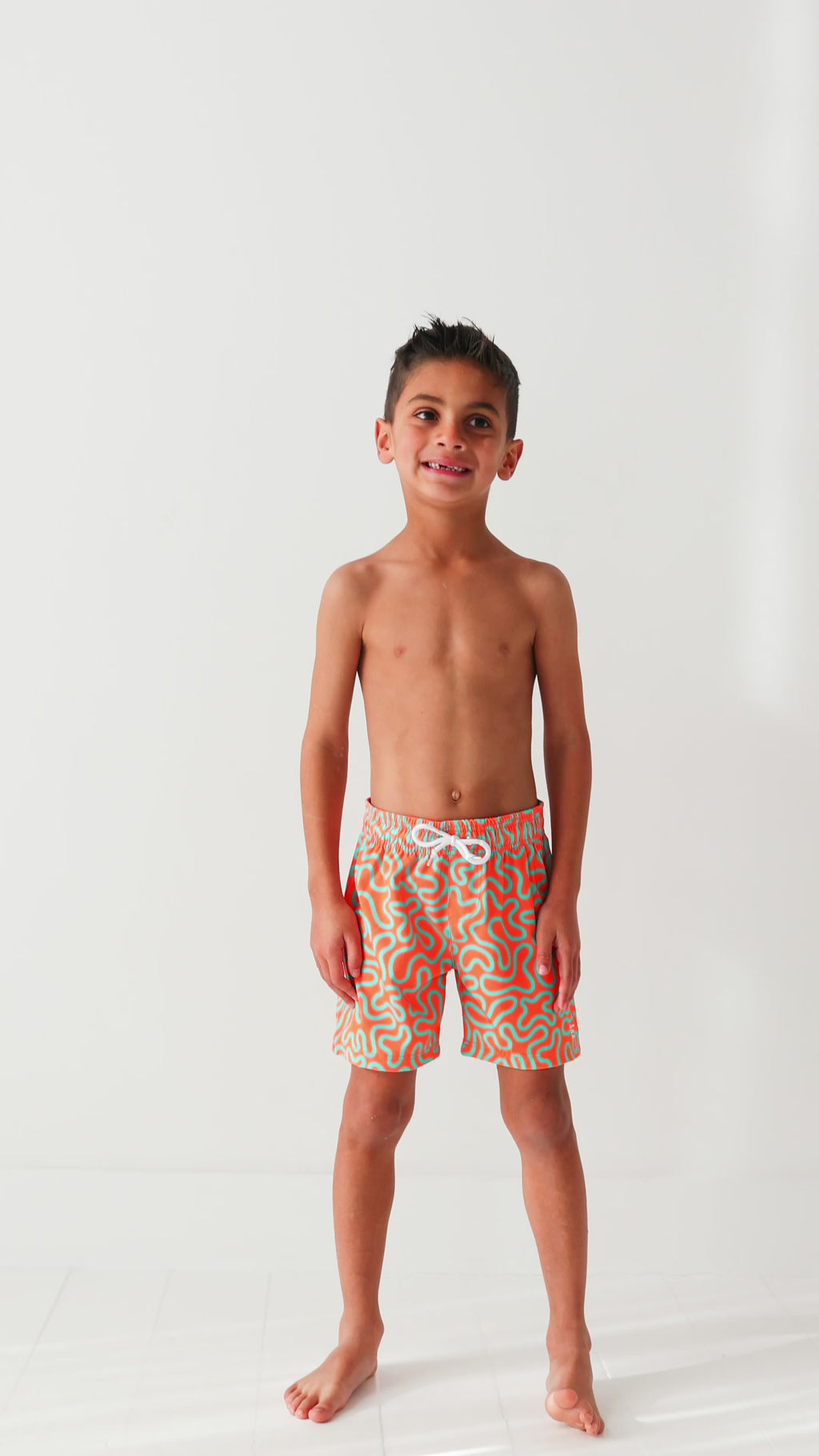 Child wearing orange and blue squiggly-patterned swim shorts on a white background