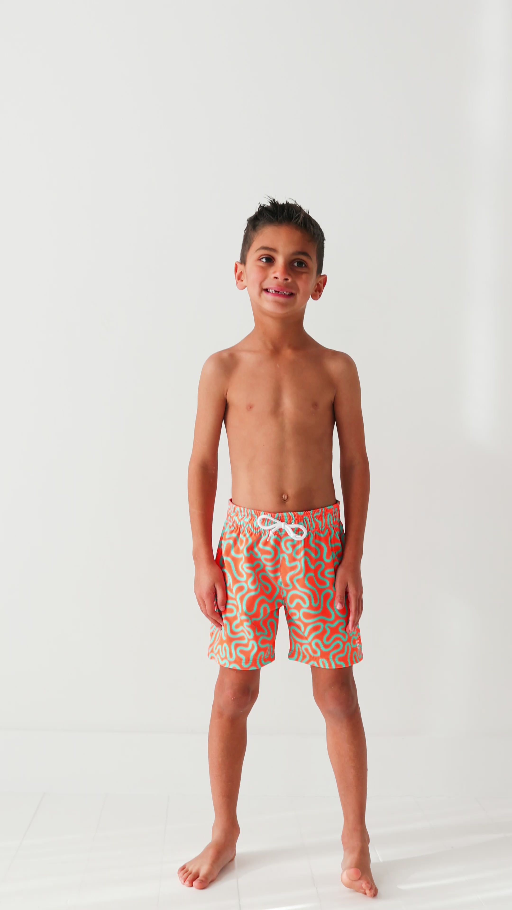 Child wearing orange and blue squiggly-patterned swim shorts on a white background