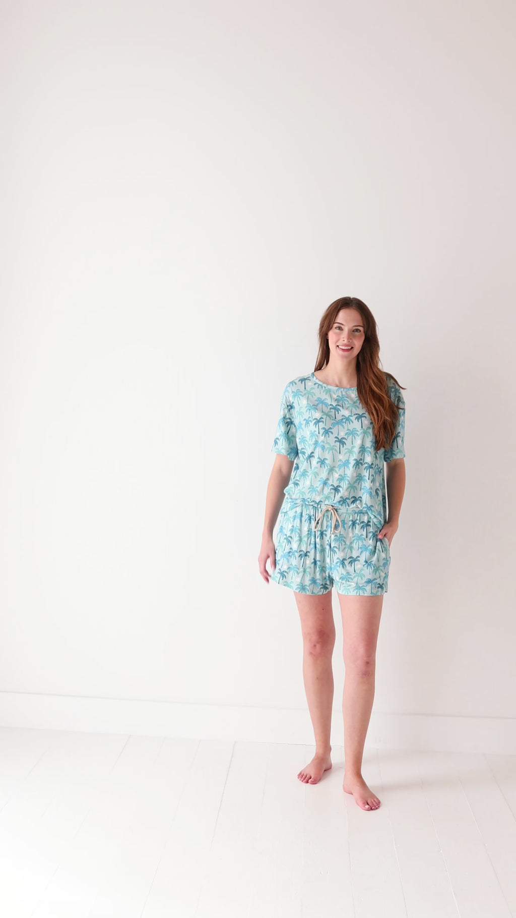 Woman wearing a blue palm tree patterned pajama set on a white background