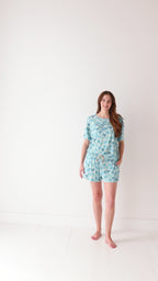 Woman wearing a blue palm tree patterned pajama set on a white background