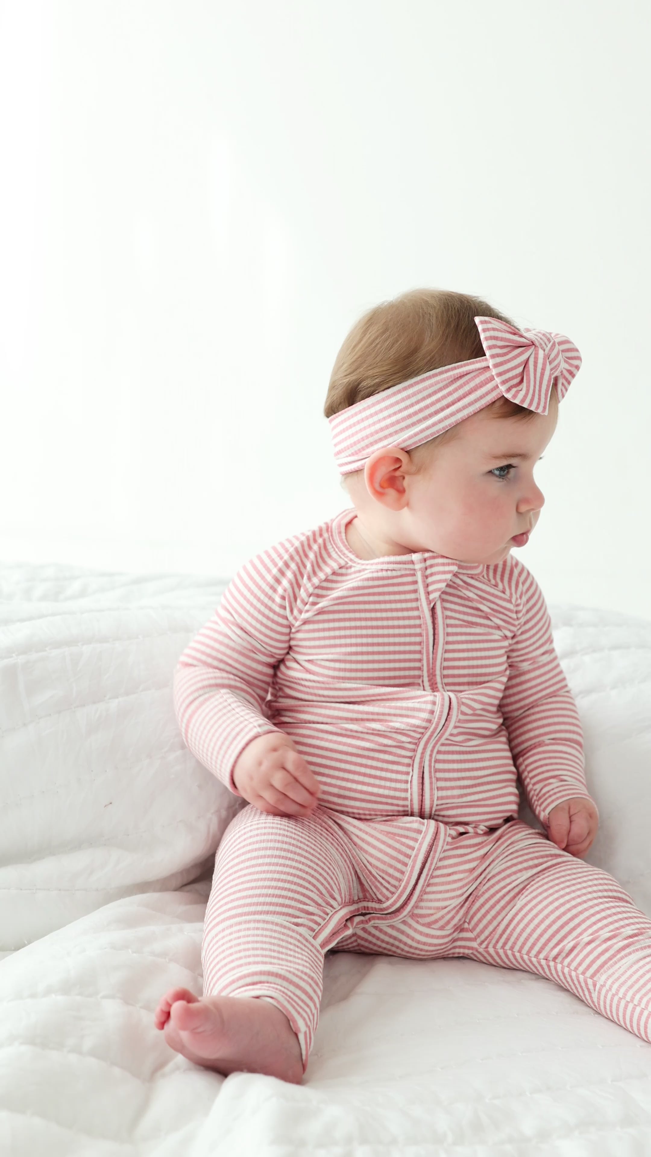 Baby wearing a pink and white striped outfit with a matching headband on a white background