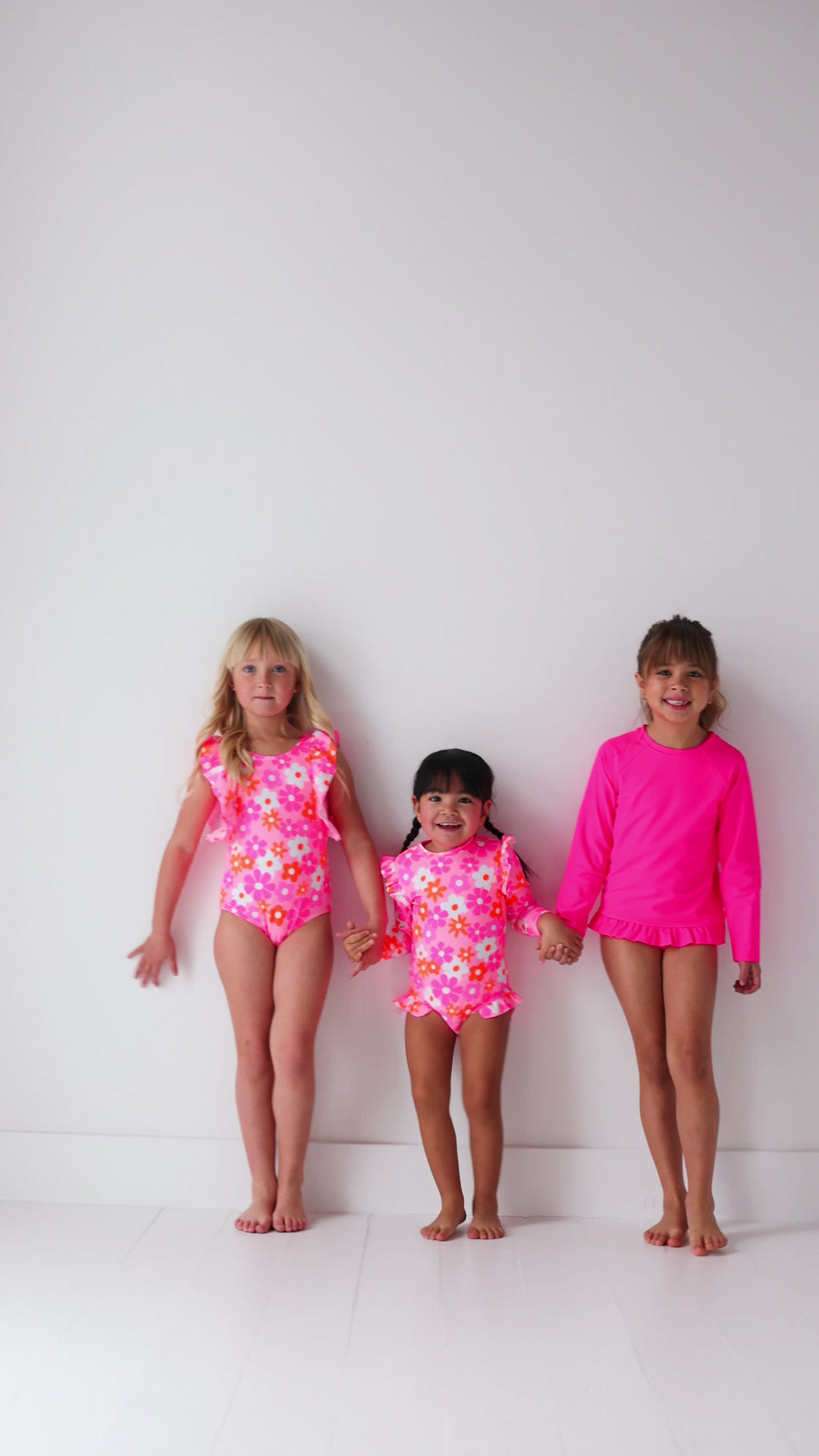 Three children wearing pink swimsuits with floral patterns on a white background
